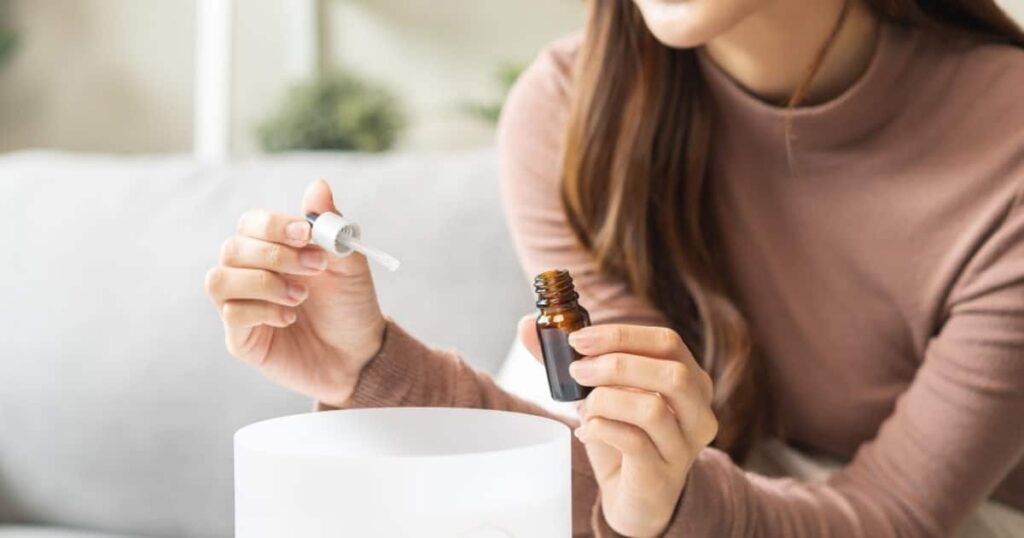 Une femme dans son salon verse une goutte d'huile essentielle dans un diffuseur.
